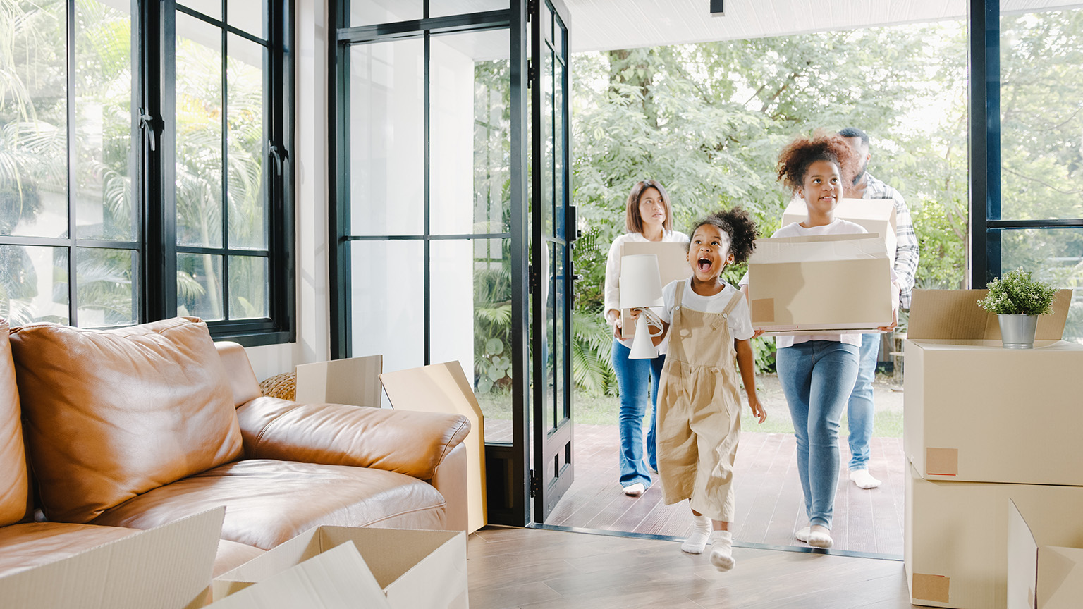 Happy African American young family bought new house. Mom, Dad, and child smiling happy hold cardboard boxes for move object walking into big modern home.